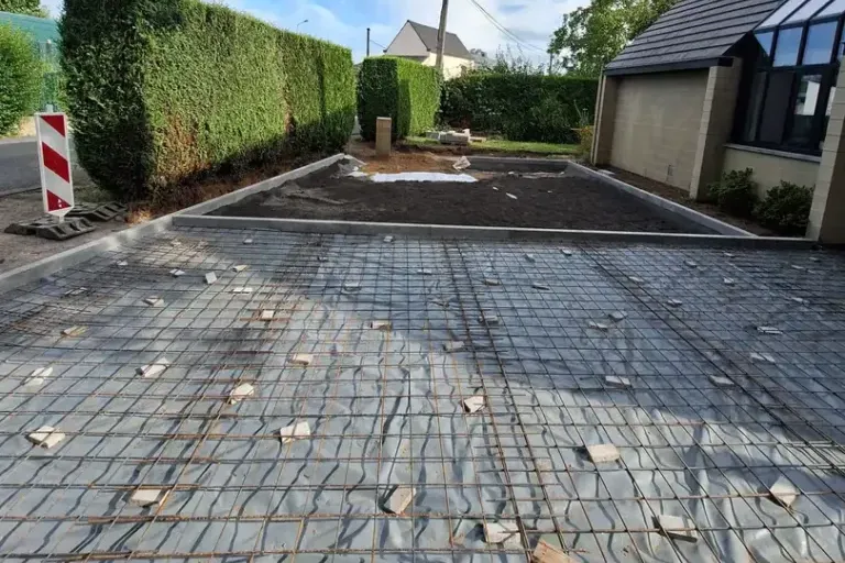 Treillis d'armature posé sur un film plastique entre deux bordures, avec une palette au premier plan, avant la coulée de l'allée