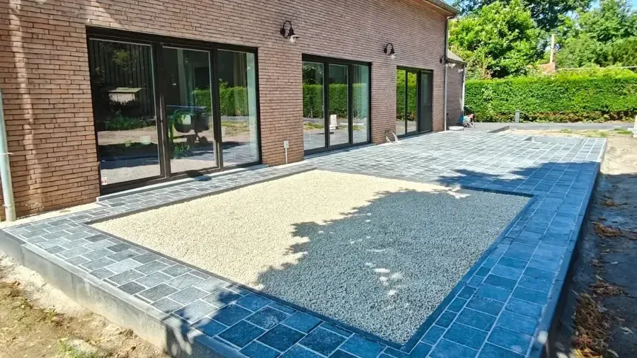 Terrasse en pavés anthracite et bleutés qui entoure une surface de gravier clair, devant les baies vitrées d'une maison en briques