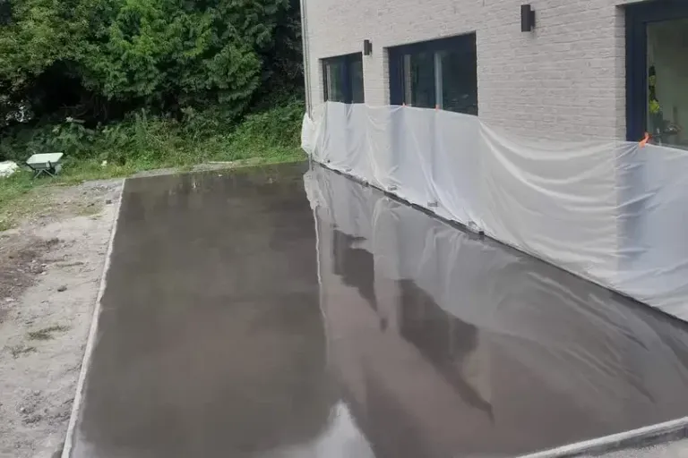 Dalle de béton fraîchement lissée, encore mouillée, contre la façade d'une maison, protégée par une bâche plastique